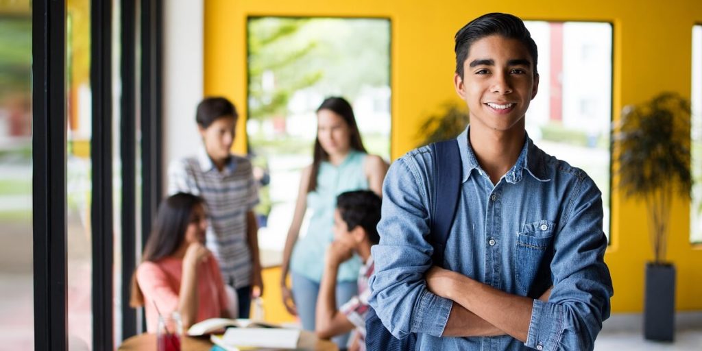 Male college student standing with arms crossed and students in background