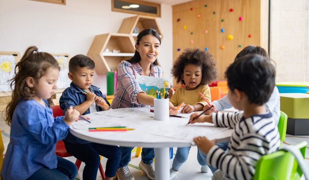 Happy group of elementary children coloring in art class with the supervision of their teacher