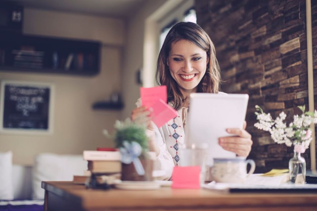 Confident, brunette female educator smiling looking over her sticky notes and tablet