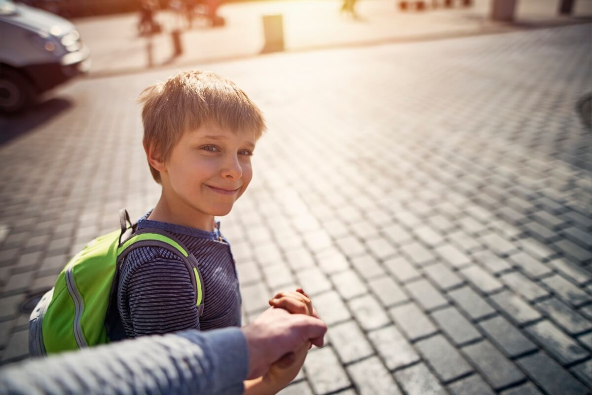 Little boy with backpack on way to school holding father's hand