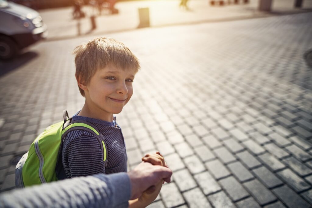 Little boy with backpack on his way to school holding father's hand.