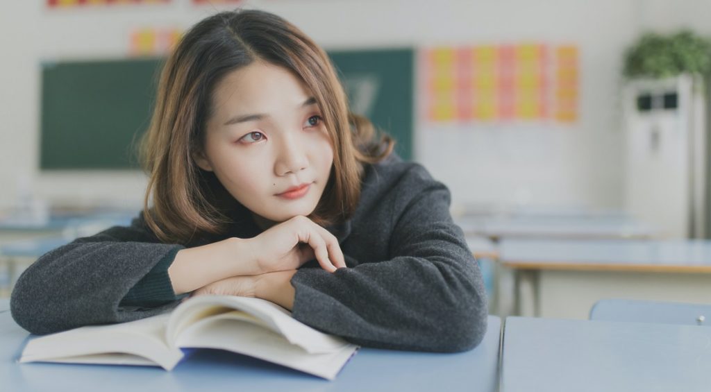 Asian student thinking at desk resting head on book