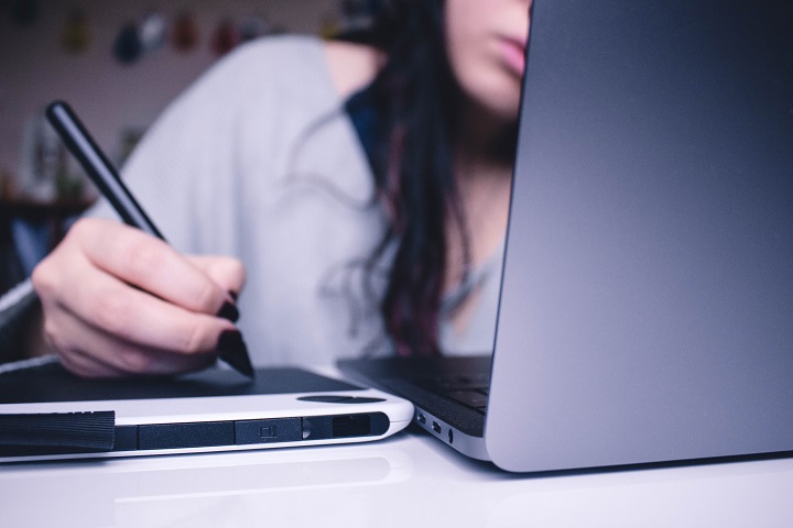 Student writing in tablet while using laptop