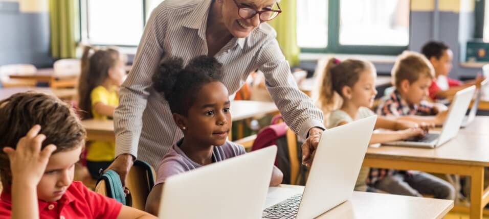 Teacher Supporting Students In Classroom with Laptops