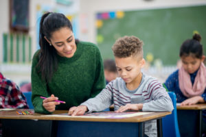 teacher helping student at desk in classroom