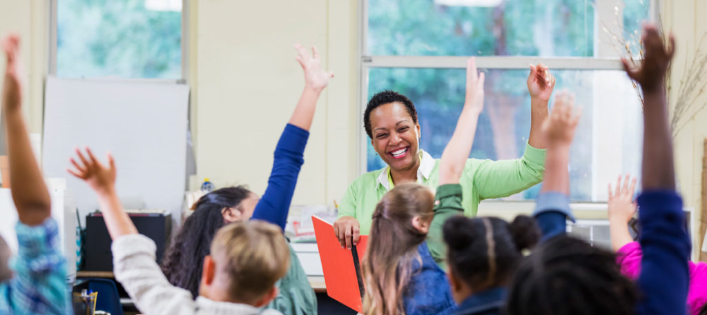 Smiling teacher in class with students raising their hands
