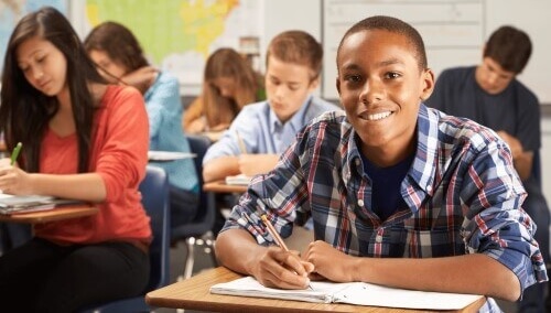 African American male grade school student in class writing in notebook