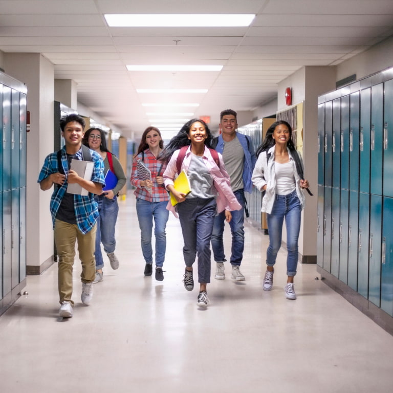 Multi ethnic cheerful teenage students running in school illuminated hallway