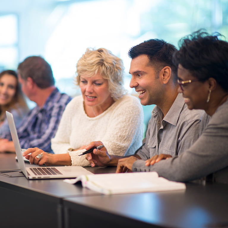 Diverse teachers in lounge comparing Vizzle to competitors on laptop