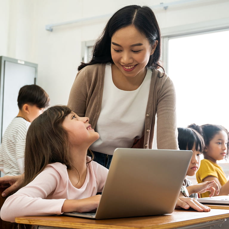 Asian teacher in technology class helping girl use laptop