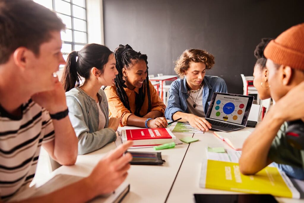 Diverse group of smiling students working on project on laptop