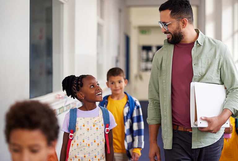 Smiling male teacher and African American elementary girl student in school hallway