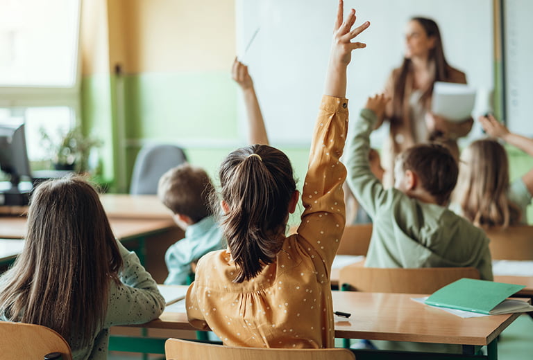 Students raising hands while teacher asking them questions in classroom