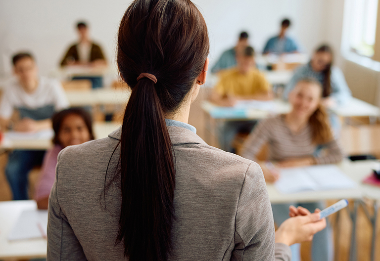 Back of female teacher giving lecture in high school classroom