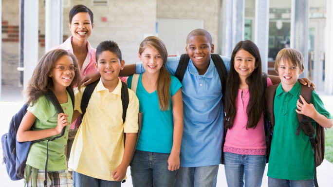 Diverse group of elementary students in hallway with teacher smiling